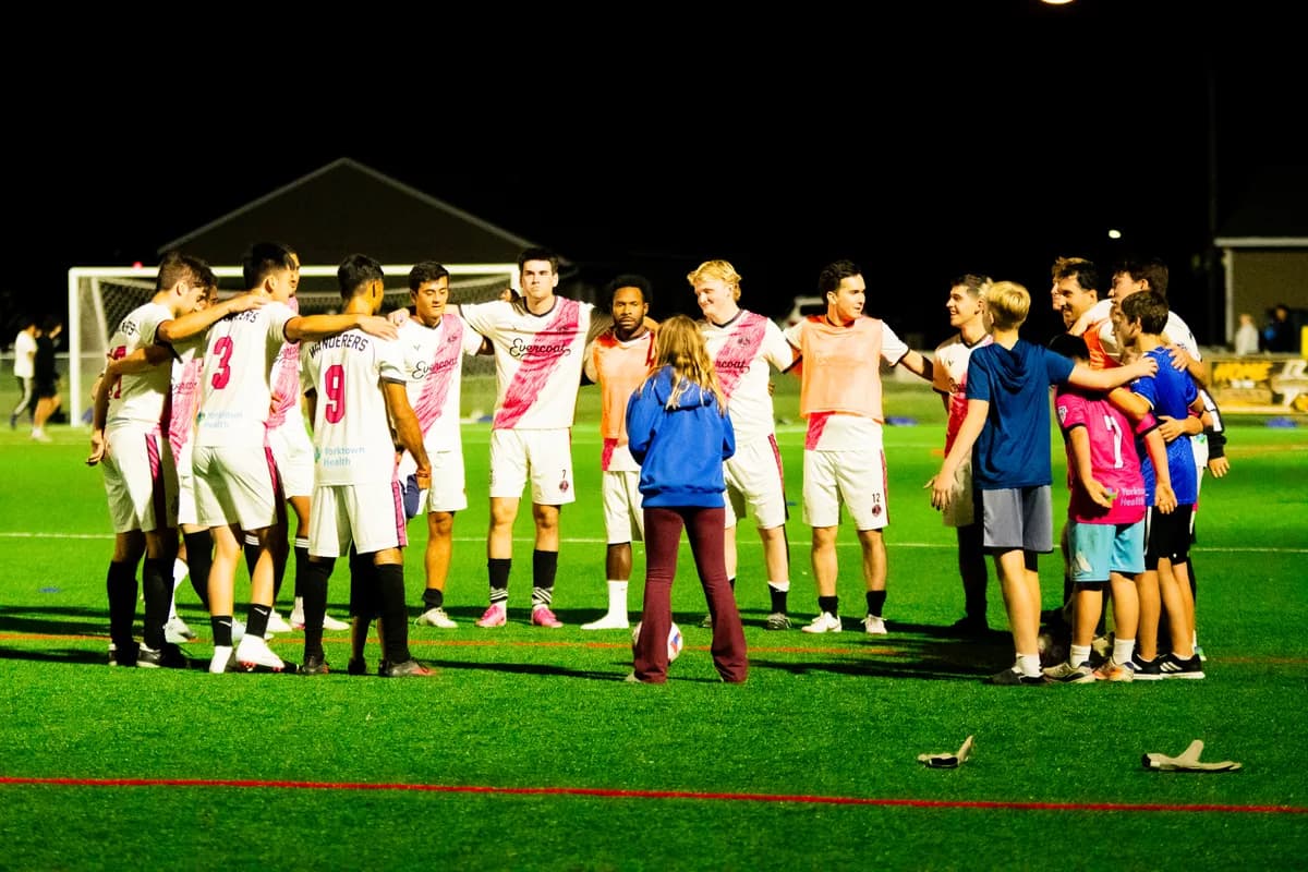 The Wanderers squad in a huddle under the lights after the home opener, with kids from the stands pulled into the circle
